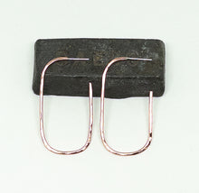 Load image into Gallery viewer, A pair of hammered rose gold hoop earrings displayed on a dark rectangular block against a light off-white background.