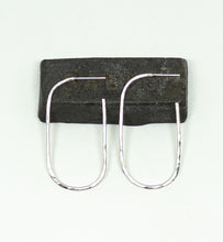Load image into Gallery viewer, A pair of silver U-shaped hoop earrings with a hammered texture, displayed on a dark rectangular block against a light off-white background.