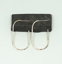 Load image into Gallery viewer, A pair of gold-toned U-shaped hoop earrings displayed on a dark rectangular block against a pale light blue background.
