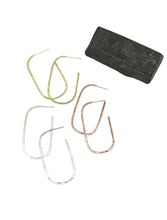 Load image into Gallery viewer, Four curved metal hoop earrings in gold, silver, and rose gold finishes, arranged on a white background next to a dark rectangular stone or block.
